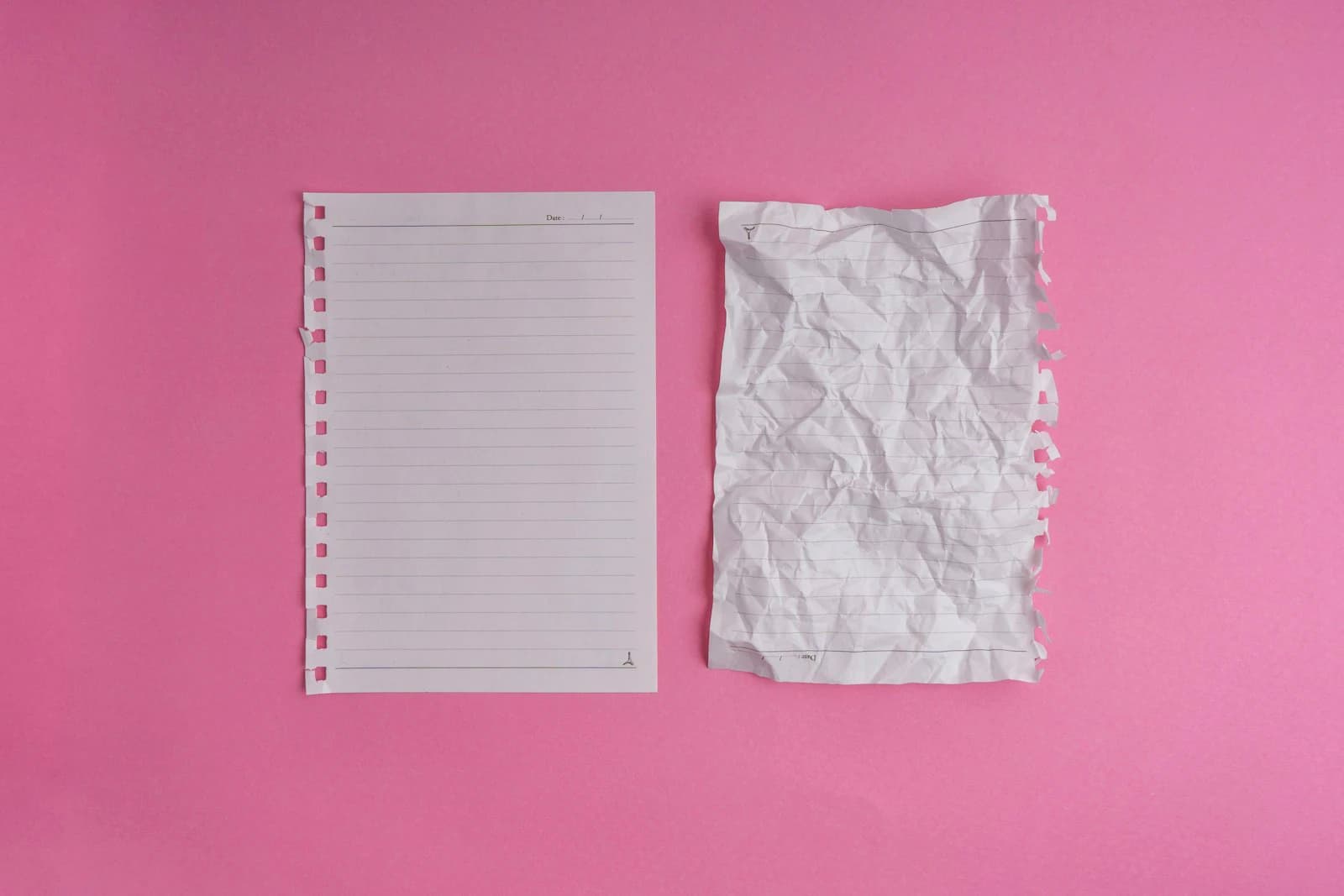 Scissors and a notepad on a pink wall
