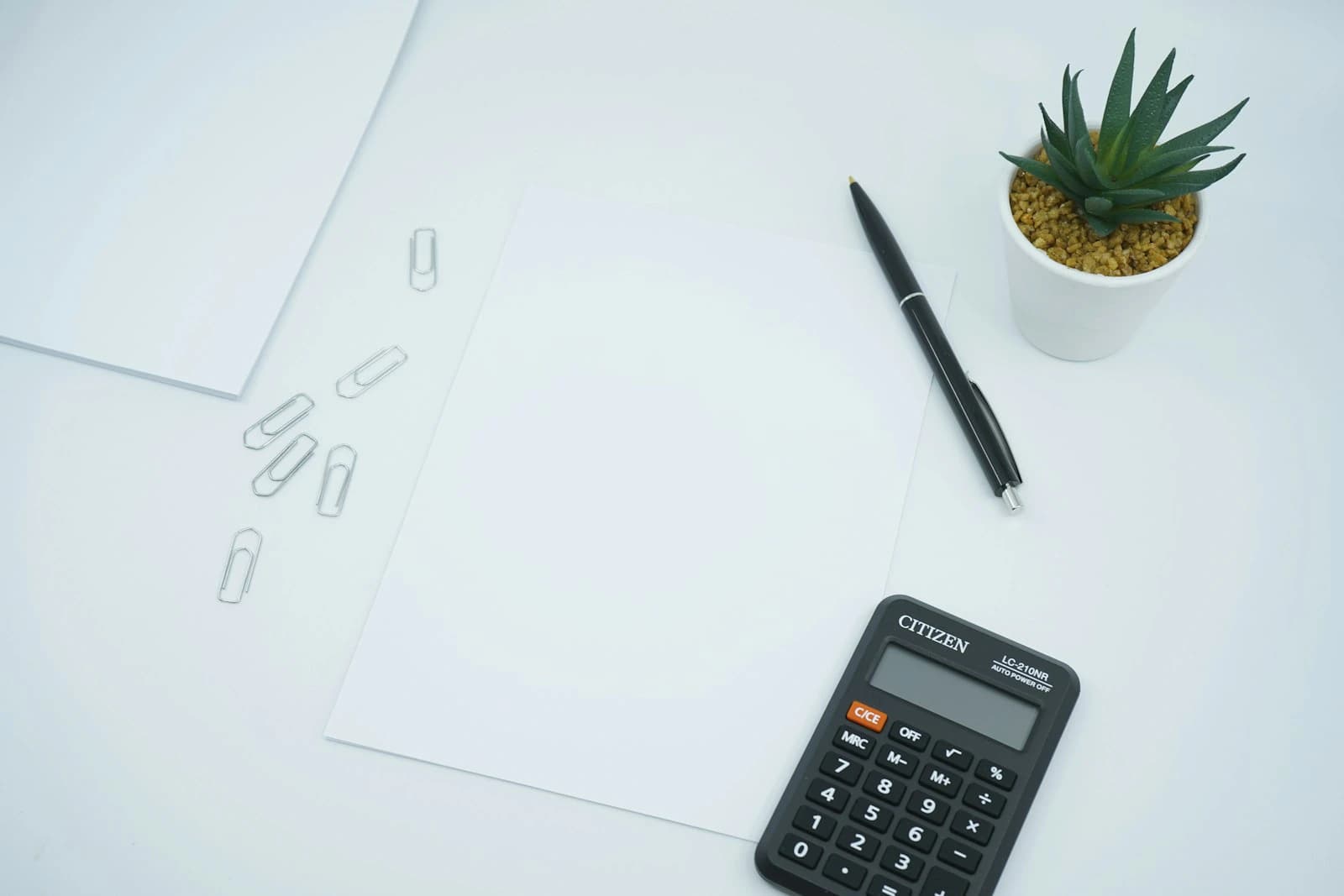 Calculator and pen beside a blank sheet of paper